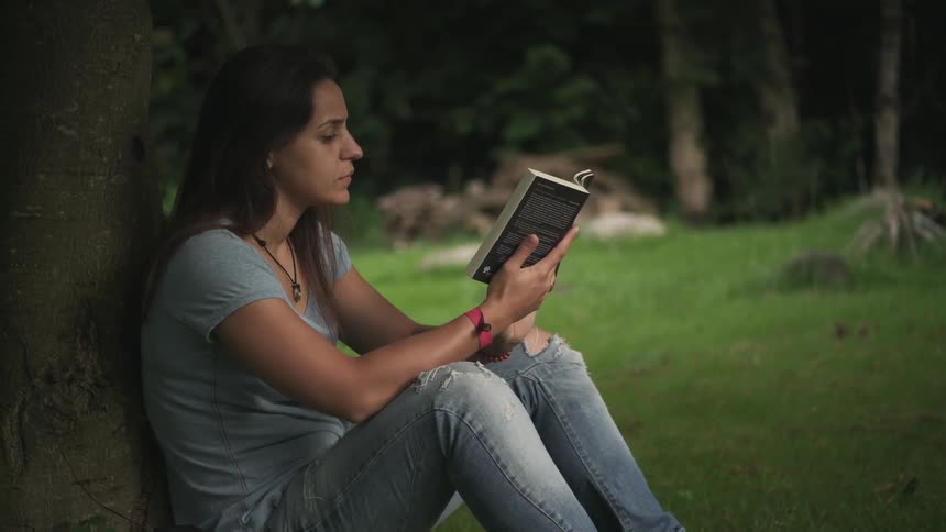 A woman sitting under a tree while reading