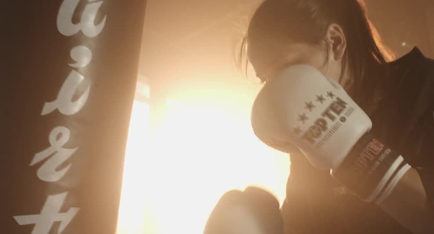 Woman wearing boxing gloves punches a hanging punching bag