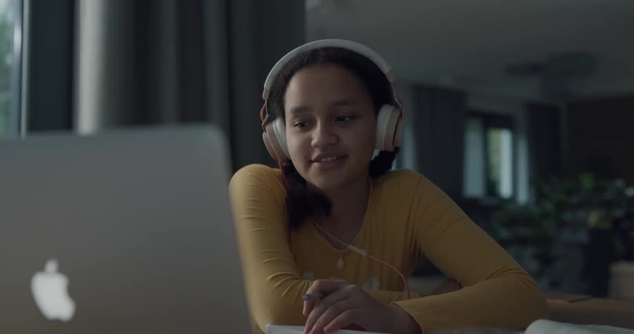 A teenage girl sits at home and video chats on her laptop