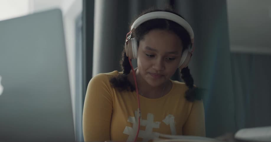 Young girl wearing white headphones reciting a homeschooling lesson in a room