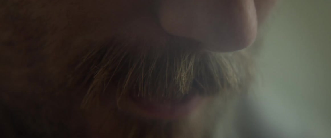 Close up of a mans face with a beard talking to someone