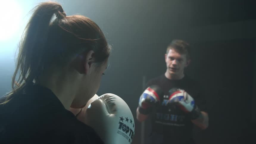 Two people are sparring in a dark area with one light