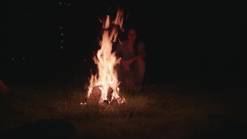 A woman sitting next to a campfire