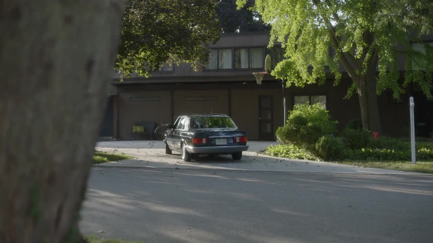 A black car pulls into a driveway in front of a house and parks