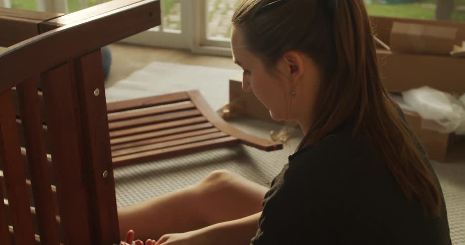 A woman sitting on a rug adjusting screws on a chair