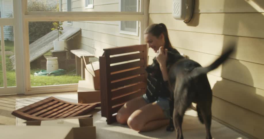 Woman assembles furniture on the porch while playing with the dog