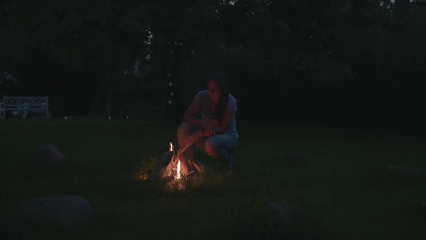 A woman squatting near a campfire at dusk