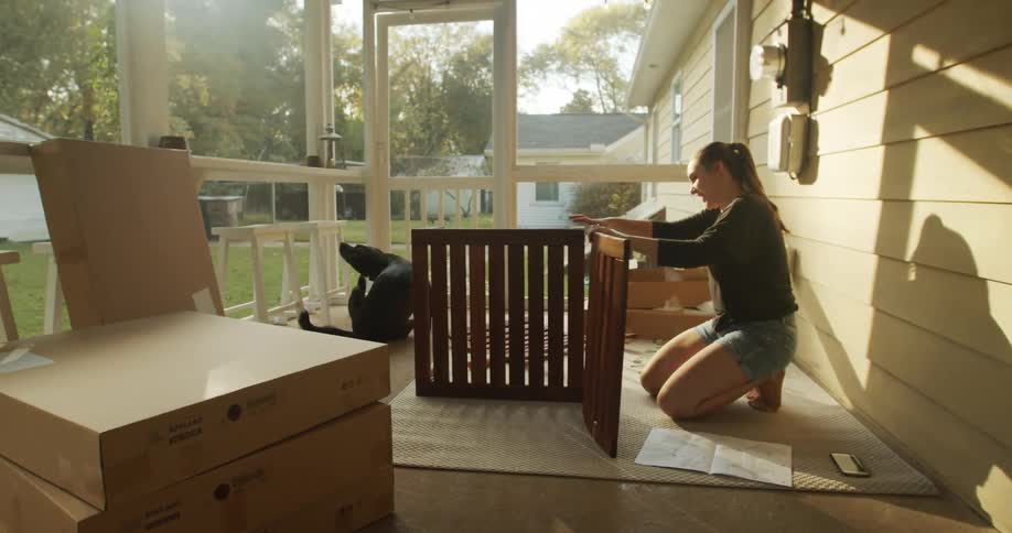 Woman assembling furniture in the porch at home with her dog at sunset