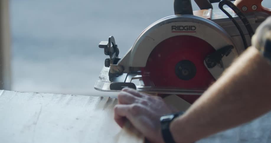 Man cutting a piece of wood using an electric saw outdoors at sunset