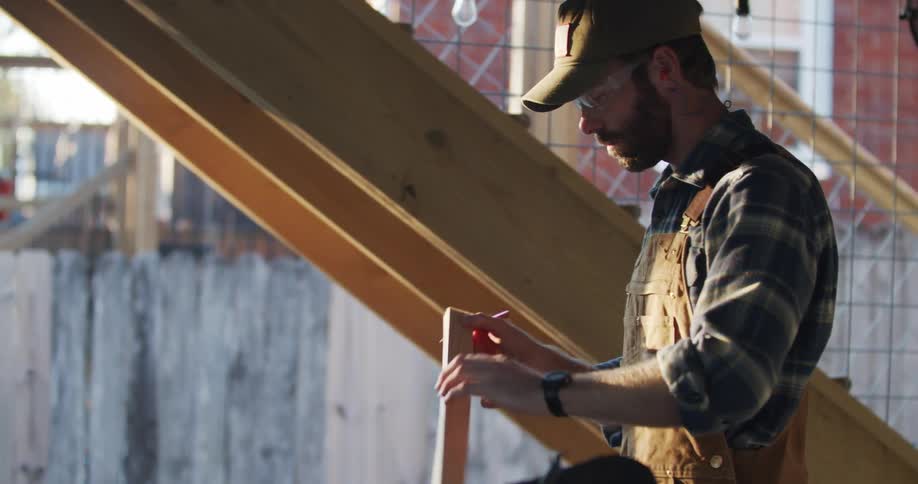 A caucasian male working at a construction site and leveling out a wood piece