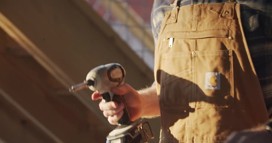 Carpenter puts a drill bit on a wireless drill outdoors at sunset
