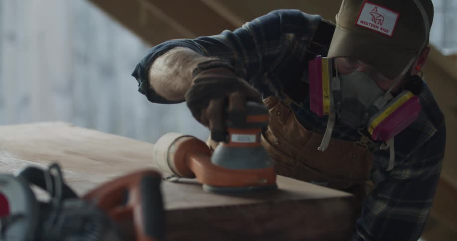 A man wearing a respirator is using a sander on a large piece of wood