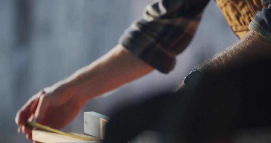 A man pulls out a measuring tape and pencil and uses them on wood