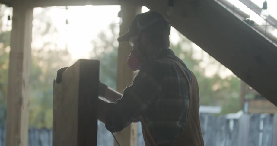 A man uses a power sander on a large board while working on building an outdoor patio