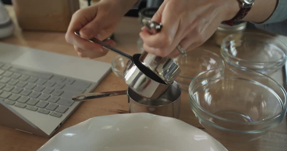 A woman arranges bowls and goes through measuring cups while preparing to bake at home in front of her laptop
