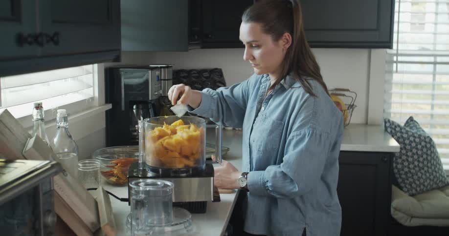 Woman cutting fruit to mix in a mixer over the kitchen countertop at home