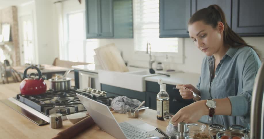Woman preparing a meal at home reading a recipe on a laptop