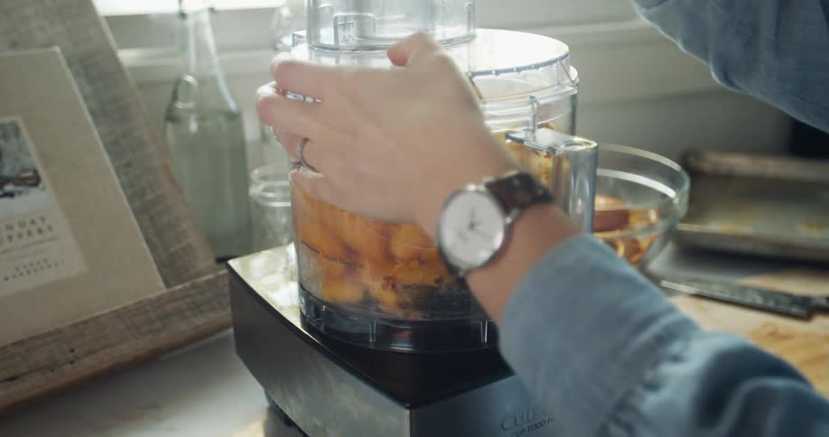 Woman uses a mixer to puree slices of cooked pumpkin at home