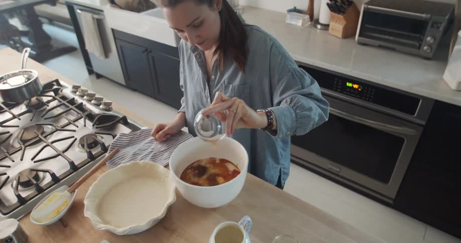 A woman adds ingredients for pie to a bowl as she cooks in her kitchen