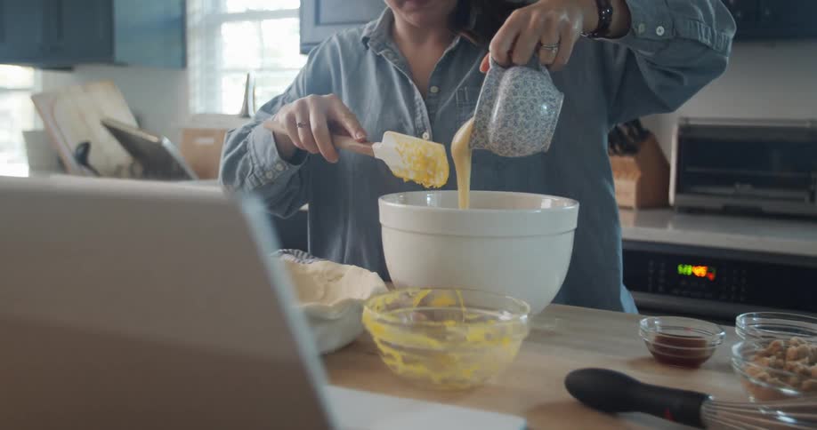 A woman pours batter into a bowl while standing at a counter in the kitchen