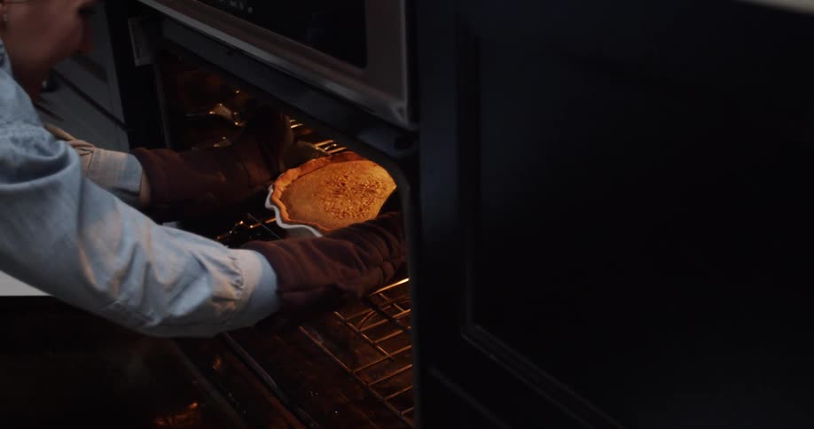 A person removes a pie from an oven with oven mitts