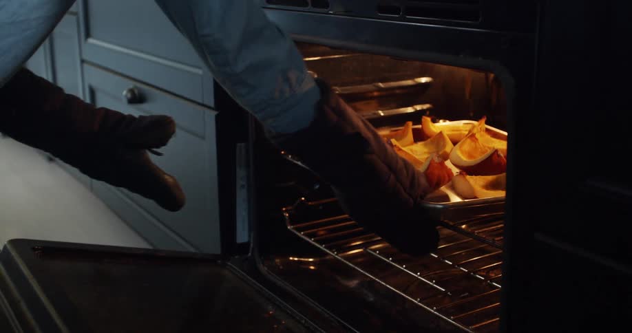 A person opens the oven door and takes out a tray with cooked pumpkin slices