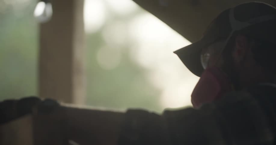 Man in goggles and with a bandanna over his mouth working with some wood as dust flies up