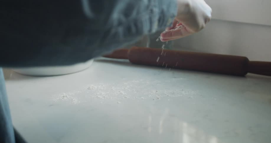 A person is sprinkling flour on the counter