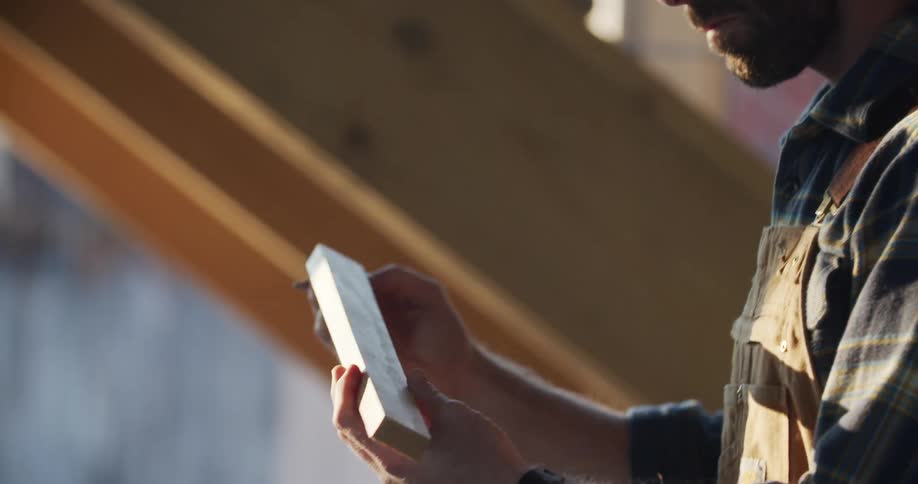 A man holds a piece of wood and marks it with a pencil