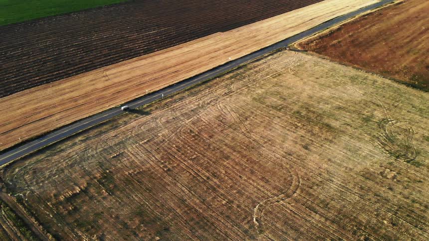 A vehicle drives past farm fields