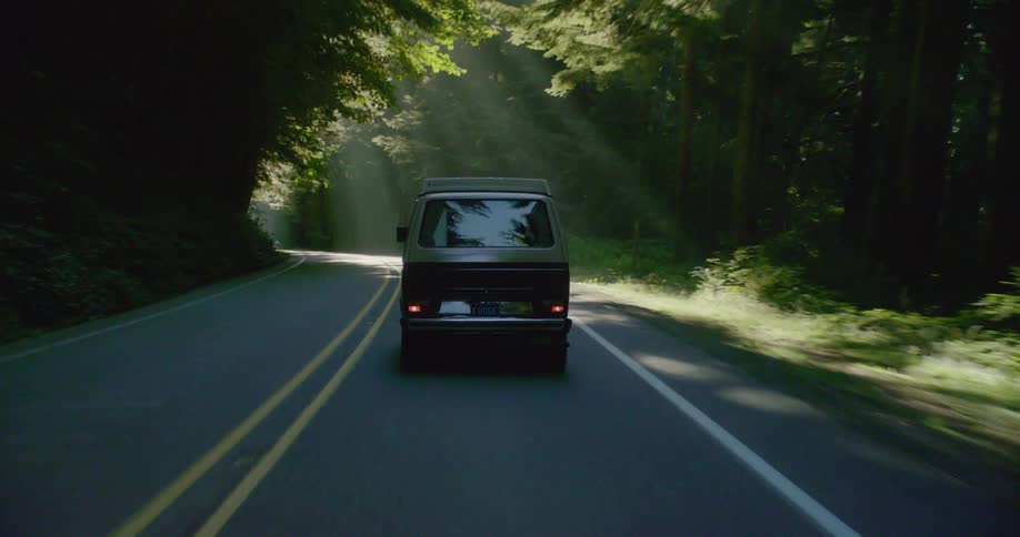 Van driving down a forest road with the sun shining brightly
