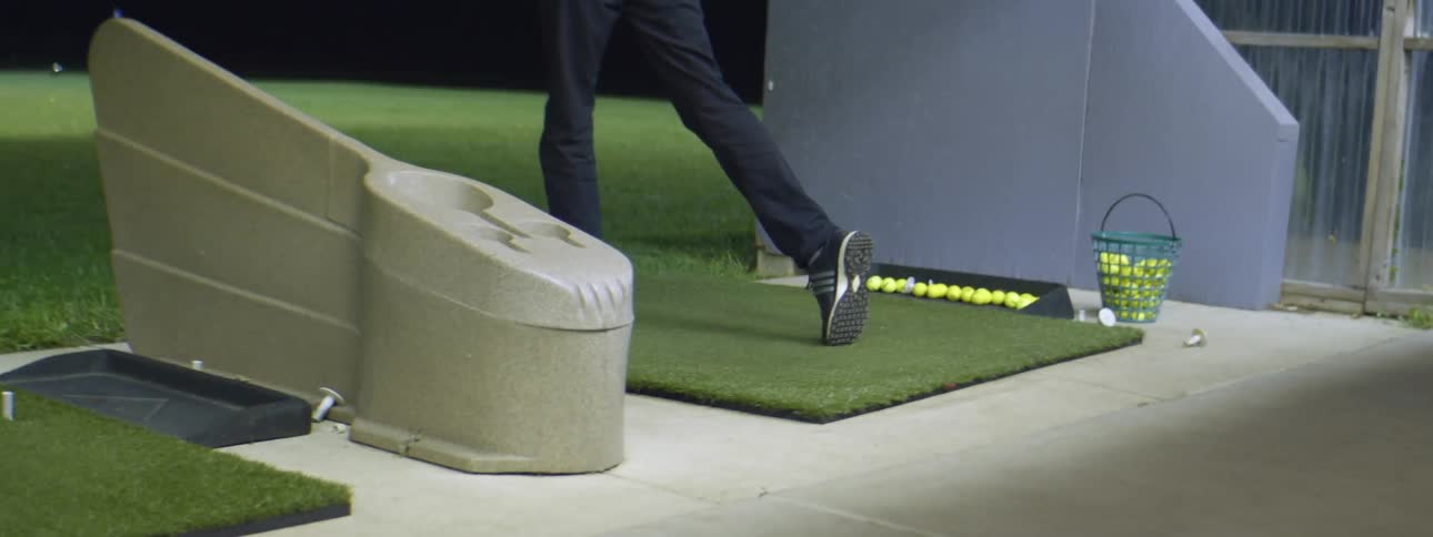 A young man practices golfing on a golf driving range at night