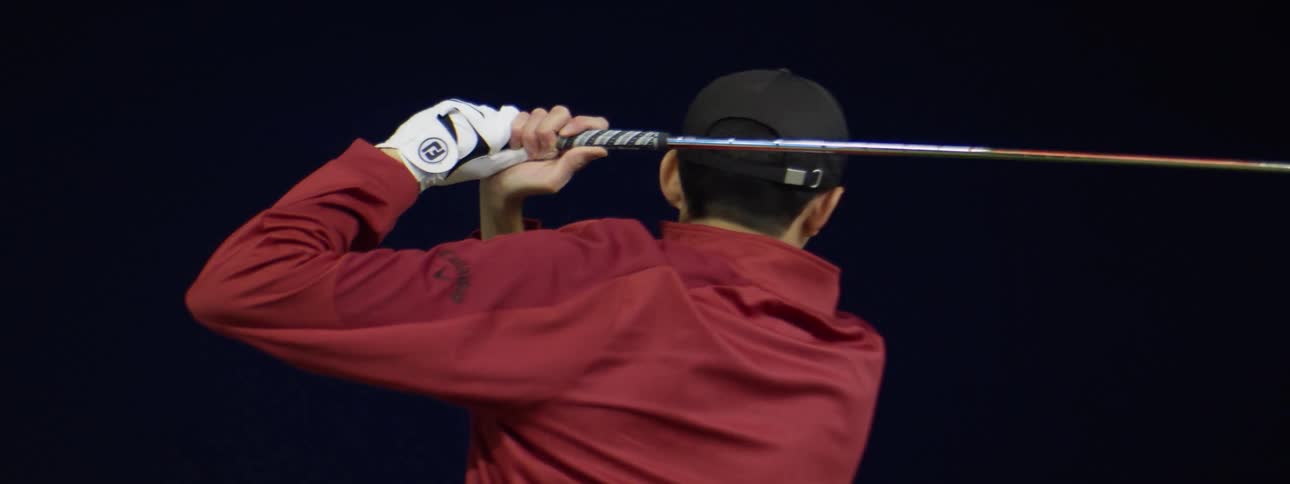 Man practicing golf swings in a golf driving range at night