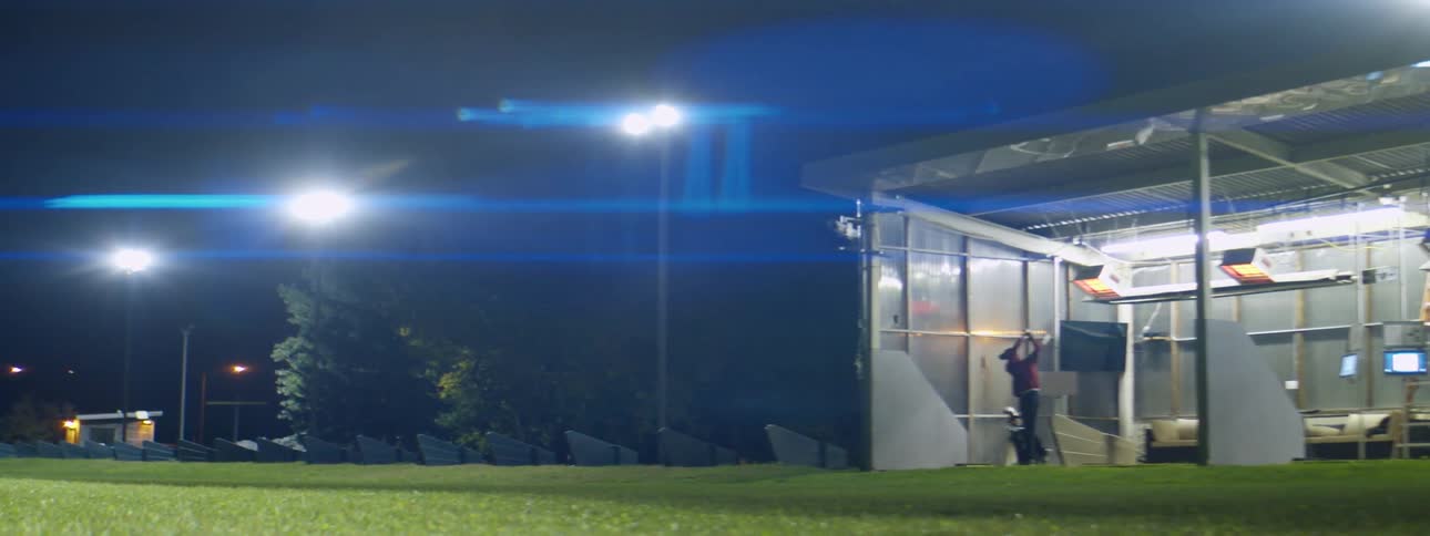 Man practices golf swings on a golf driving range at night