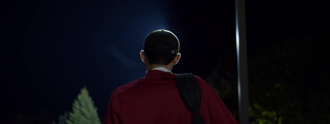 Man walking and carrying a bag with golf equipment outside on a golf course at nighttime