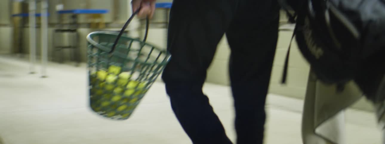A man carries a basket full of golf balls and golf clubs as he walks onto the driving range