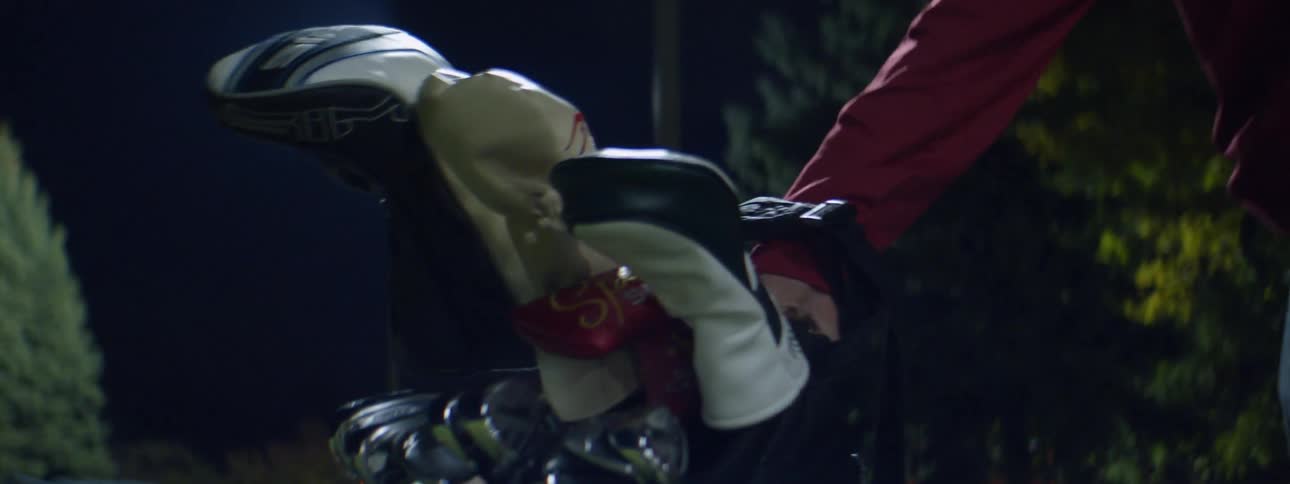 Man places a golf bag filled with golf clubs on the ground at night