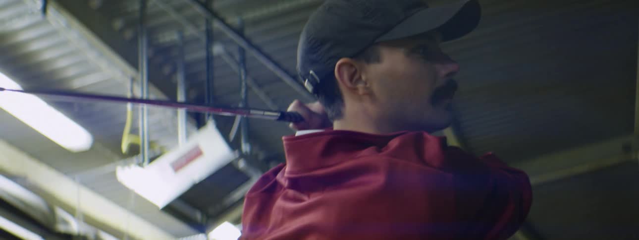 A male golfer hitting a golf ball at a driving range at night