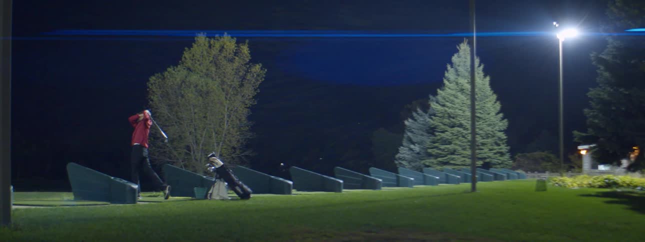 A man practicing golf at night at a golf range