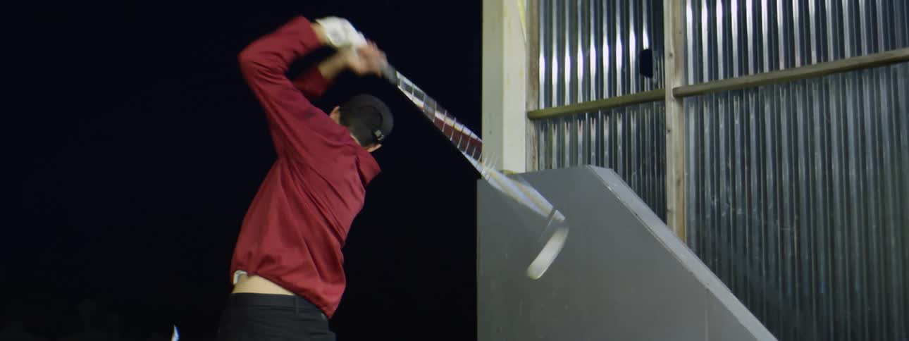 Man swings a silver golf club at a golf course at night