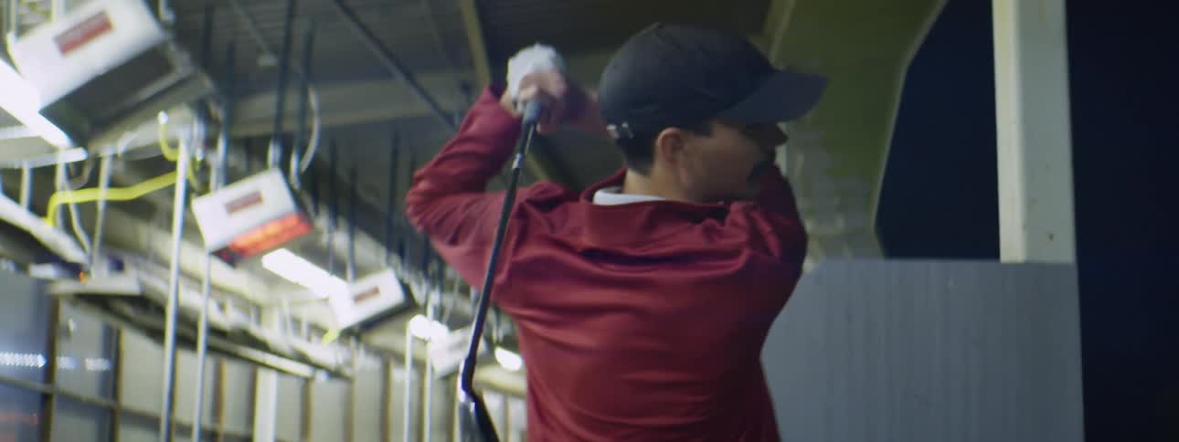 A man with a hat and a jacket swinging a golf club
