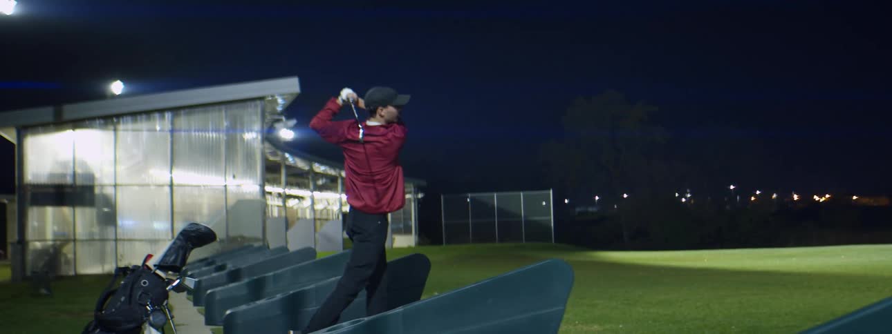 Man practicing golf swings on a golf driving range at night