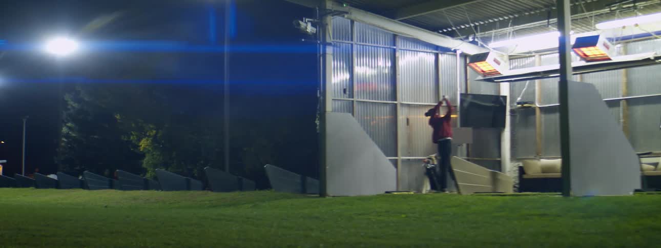 A golfer hitting a golf ball on a driving range at night