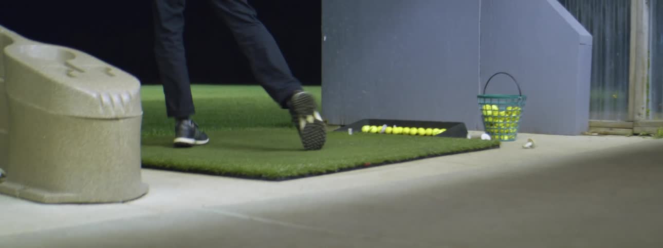 A person hits yellow golf balls with a golf club outdoors at night