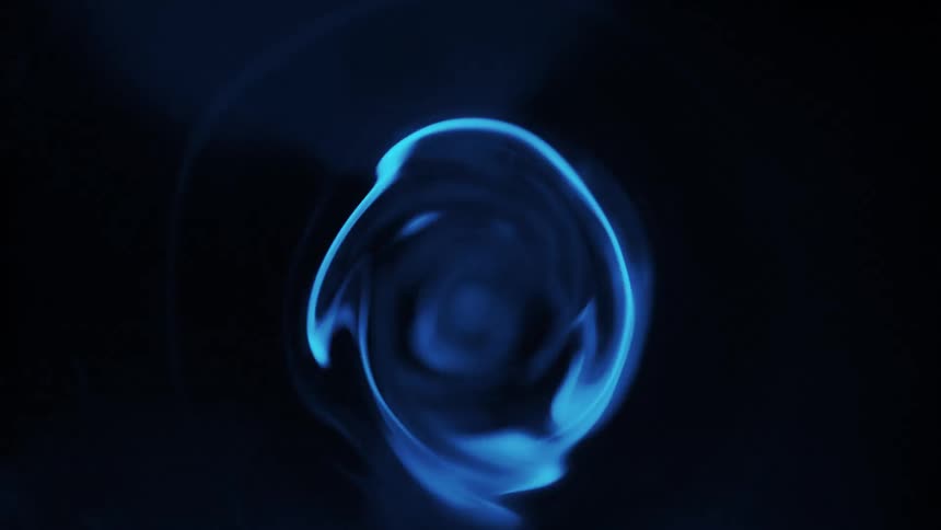 Electric blue edged circular mass rotates against darkness