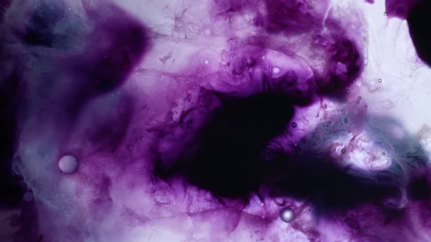 Purple liquid ink spreading in water forming abstract shapes