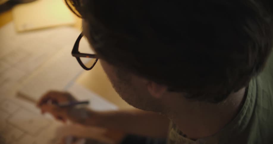 A man uses a pencil and appears to be writing on a paper blueprint