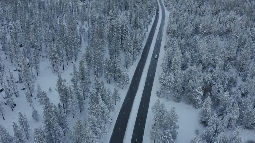 Car drives down highway through snow covered forest trees with mountains on the horizon