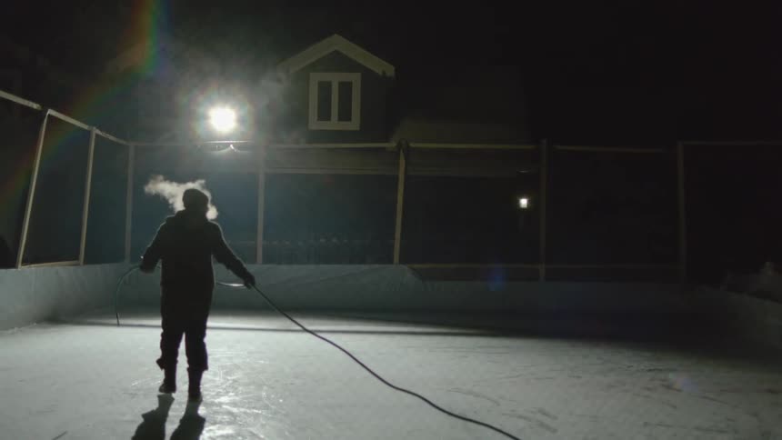 A man carries a hose onto an ice rink he created behind a house