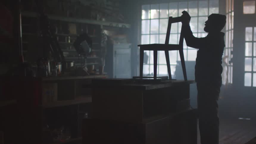 A man fixes a chair in a a dark storefront